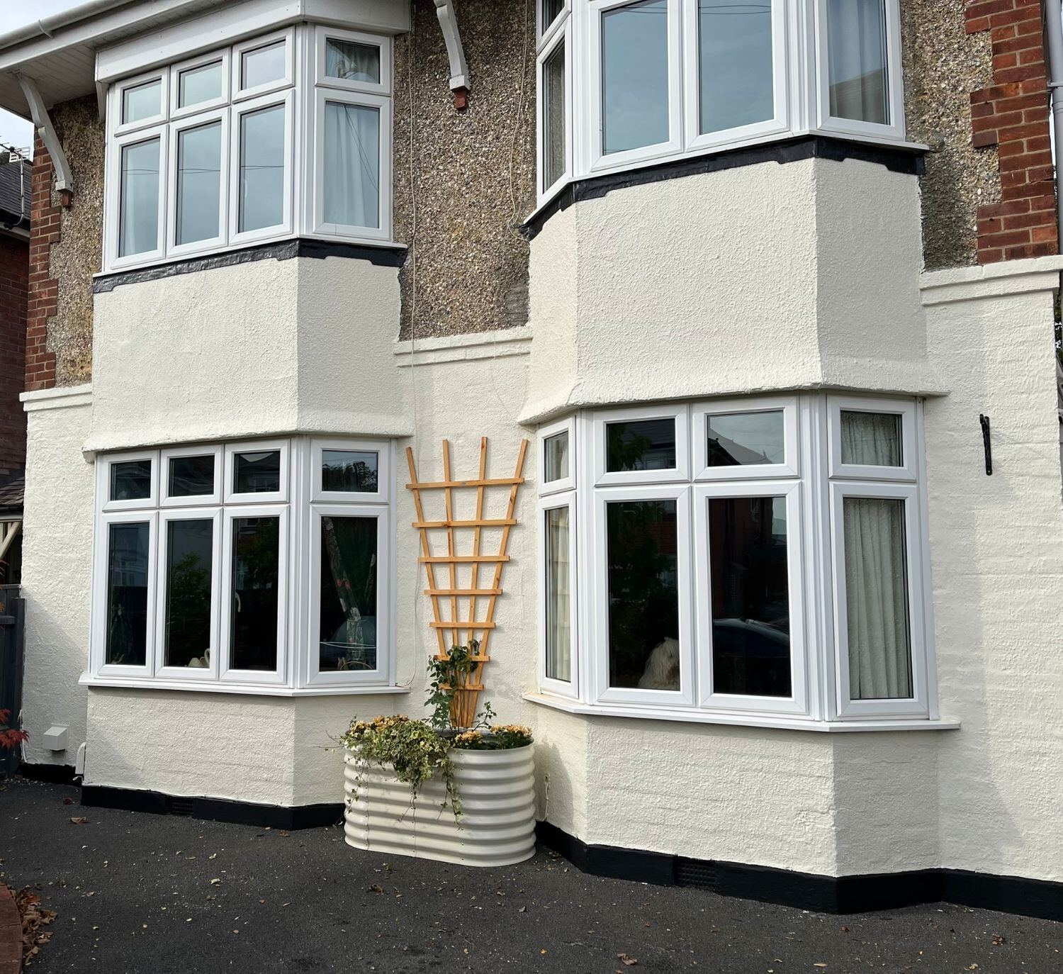 Front of a house with bay windows, the render painted off-white and the plinth black