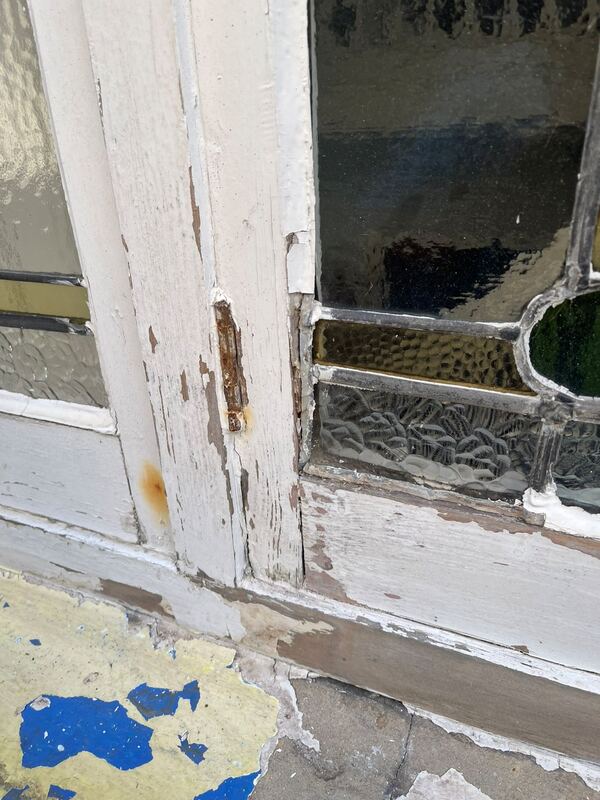 Corner of an old timber window before work, with flaking paint, bare wood and a rusty hinge