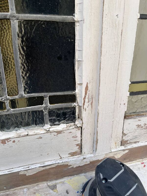 Close-up of cracked putty and peeling paint around a leaded glass panel