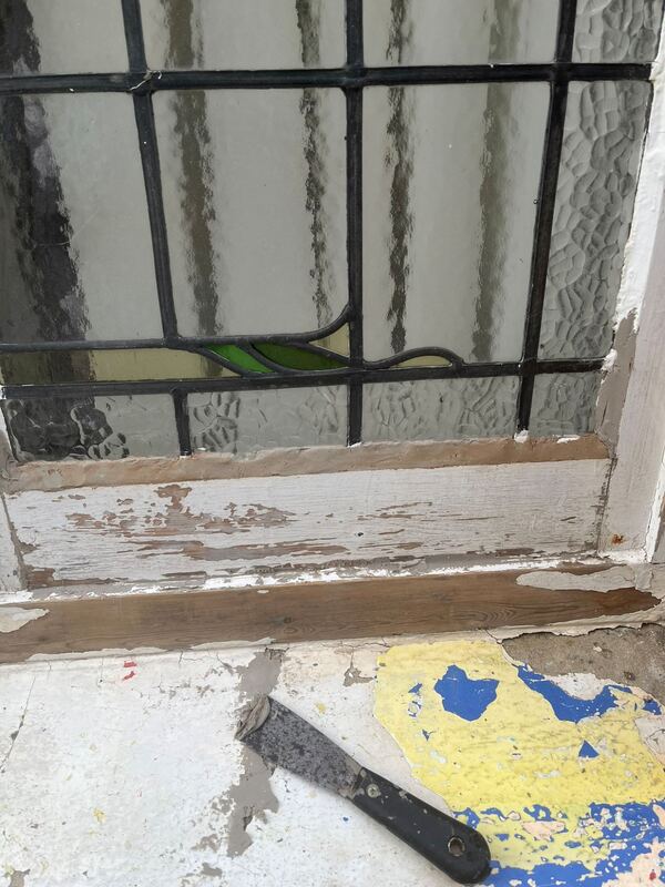 Bottom of the window partway through prep, paint scraped back and fresh filler along the glass, with a filling knife on the sill